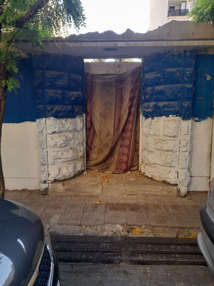 درگاهی با پردهٔ پارچه‌ای و ورق‌های فلزی آبی و سفید در دو سو — A doorway closed by a cloth curtain, flanked by blue and white metal sheets